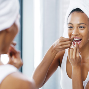Woman smiling while flossing teeth in bathroom